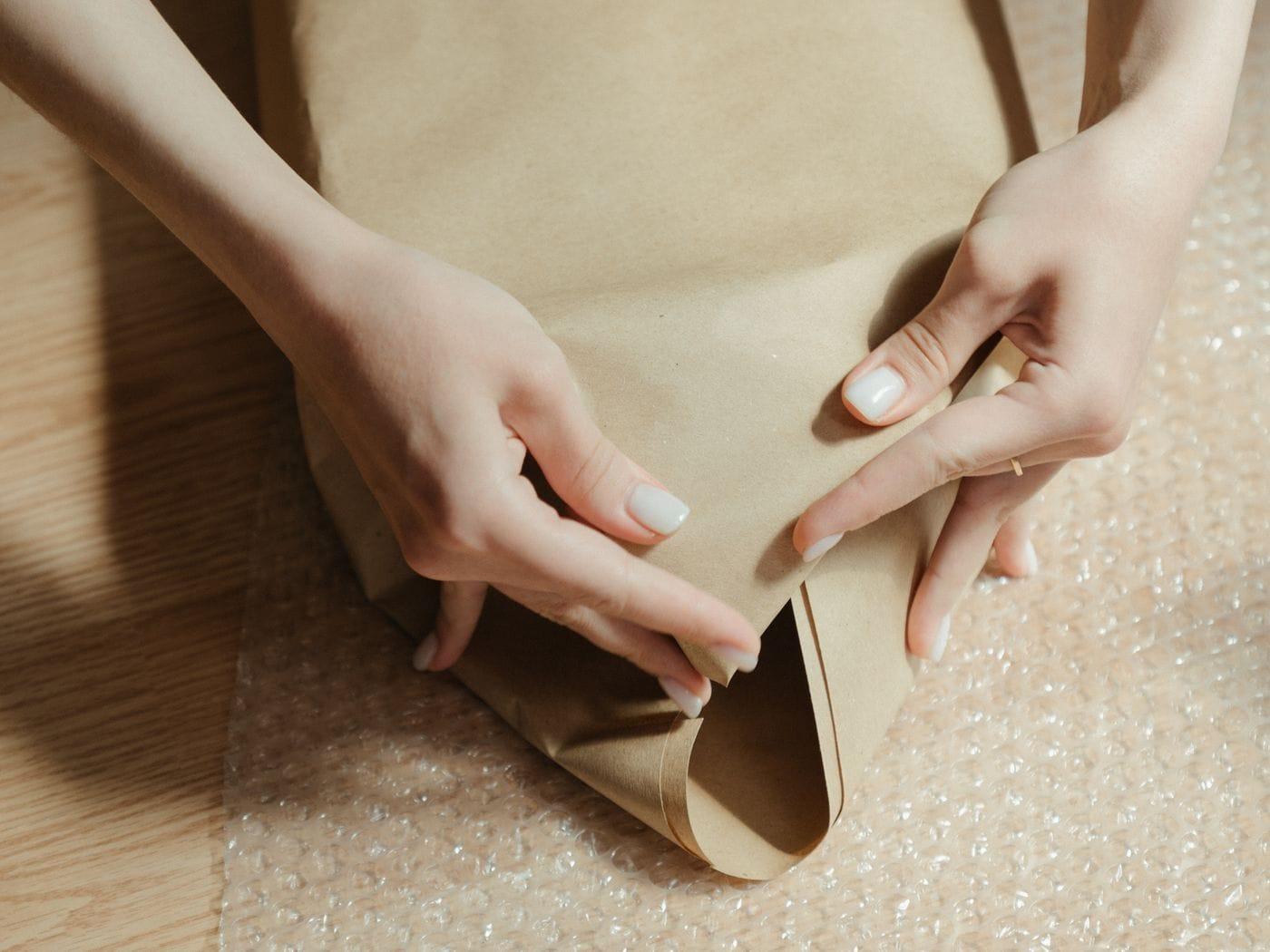 Hands folding kraft paper around a package over bubble wrap.