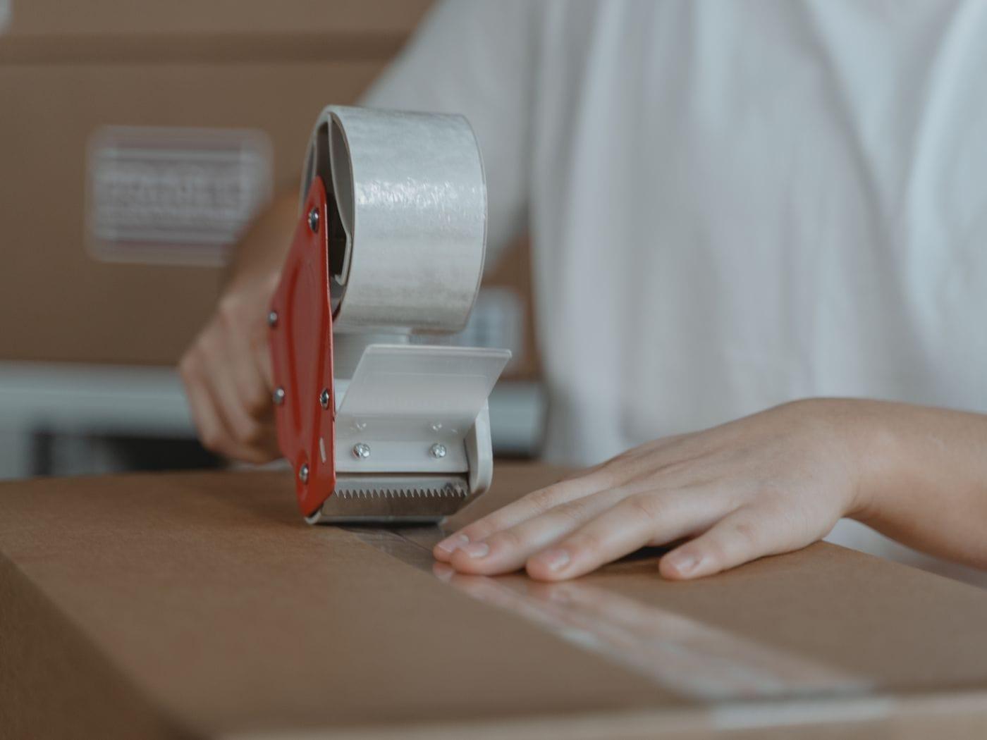 Hands taping a cardboard box shut.